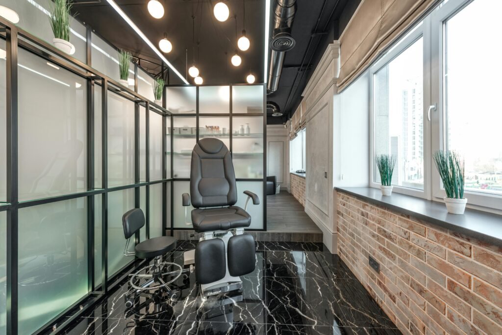 A modern massage chair placed in a stylish room with sleek black marble flooring, frosted glass partitions, and large windows adorned with minimalist potted plants. The chair is ergonomically designed and adds a sophisticated touch to the decor.